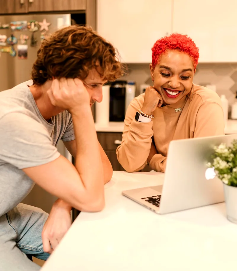 Casal sorrindo, olhando juntos para o notebook, organizando as finanças em casa